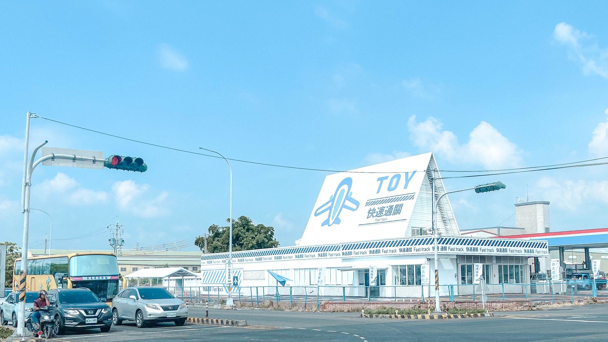 快速通關玩具店外觀：航廈造型的白色三角量體，TOY 與紙飛機招牌，藍白斜紋雨遮印滿「快速通關 Fast track」字樣，藍天下像一座迷你機場